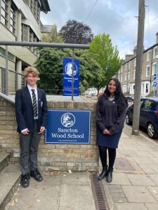 two students standing infront of a sancton wood school poster